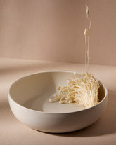 A beige Stoneware Shallow Serving Bowl with a capacity of 60 oz, displayed against a neutral background with a small amount of food items like pasta or noodles in it to showcase its size and shape.